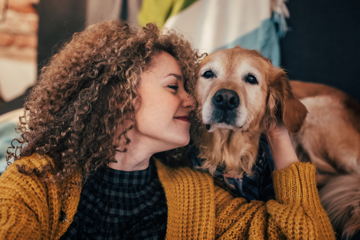 Woman with curly hair cuddling a golden retriever on a cozy couch, both looking content and relaxed.